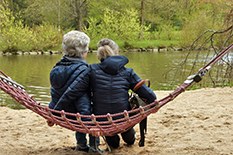 Jongedame zit met een oudere dame op een hangmat kijkend naar een meertje